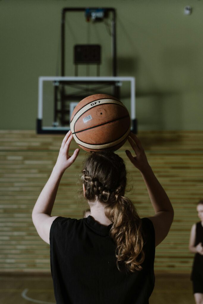 A young female basketball player aiming to shoot during a practice game indoors.